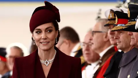 Princess of Wales in a maroon suit and hat greets a line of dignitaries at a welcome ceremony in London for the Emir of Qatar