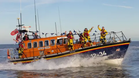 The Freddie Cooper all-weather lifeboat - an orange and navy blue vessel gliding across the sea with crew members onboard.