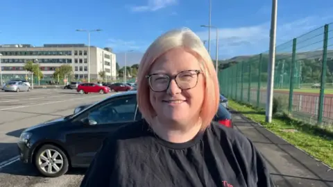 Tina wears a black T-shirt and has blonde hair with pink highlights and wears glasses and is pictured outside Aberdare community school