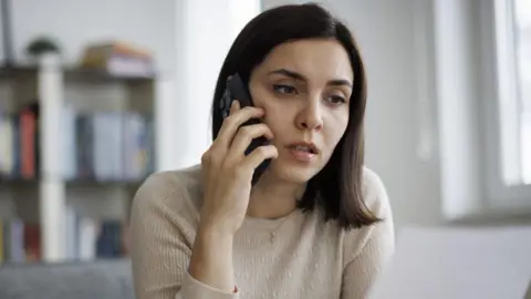 Getty Images Woman holds smartphone to ear and looks concerned