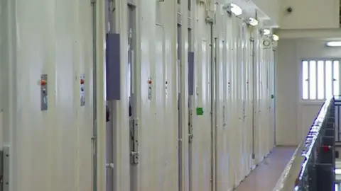 BBC Cells at a young offender institution. The doors are all closed and light in colour. 