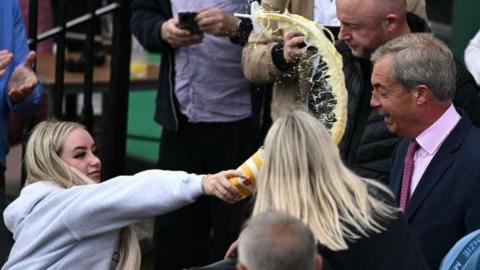 A woman throwing a milkshake at Nigel Farage while he is campaigning in Clacton-on-Sea