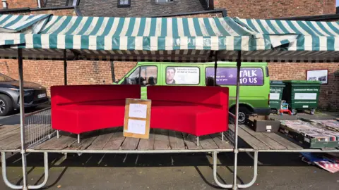 The red sofa on a market stall at Cheadle's outdoor market with a sign on top which reads 'red sofa, £29.99'