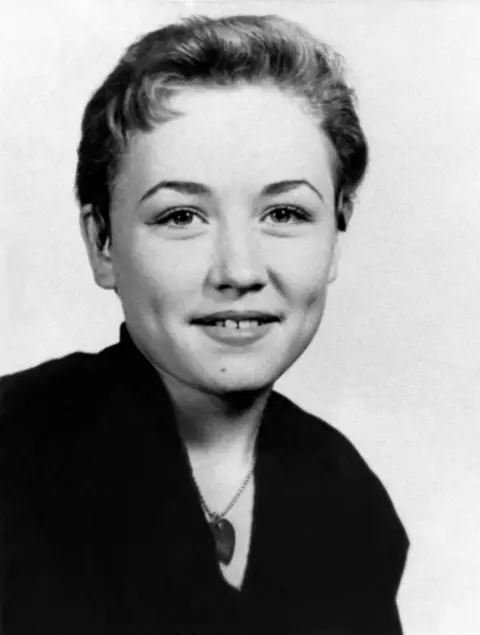 Nancy Barr/MediaPunch via Alamy Dolly Parton, age 14, with short hair and a slight smile, in a black and white high school portrait., She wears a dark shirt and pendant necklace.
