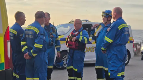 HM Coastguard A group of rescuers in blue and yellow uniforms by the sea