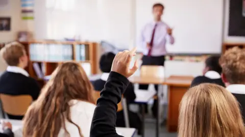 Getty Images Female Student Raising Hand To Ask Question In Classroom.