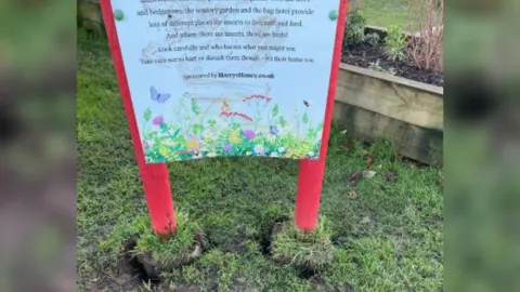 A sign with a poem on it has been placed back into the ground after being kicked over. There is mud on the sign where it has been vandalised. 