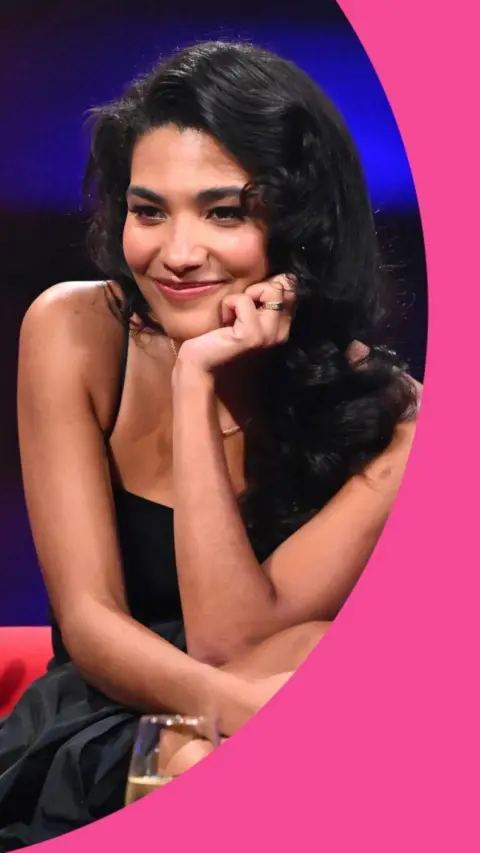 A woman, Olivia Dean, wearing a black strappy dress and long dark hair.