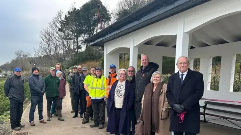 Lyme Regis Town Council A group of people - councillors, staff and members of the public - posing in front of an open-fronted pavilion.