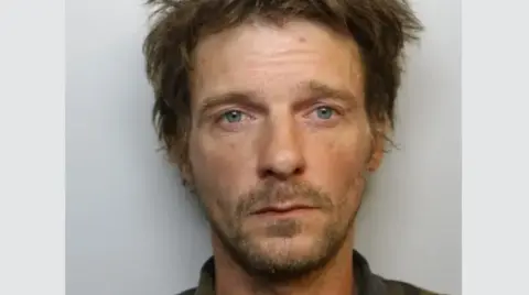 Avon and Somerset Police Mugshot of Jack looking into the camera with a blank expression. He has blue eyes and brown hair. 