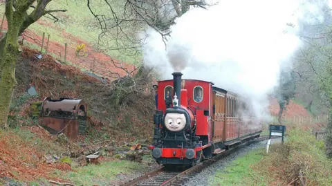 Getty Images A red train is seen climbing through the woods on the approach to Nant Gwernol with a Tywyn - Nant Gwernol service. April 2004