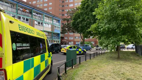 Ambulance to the left, with a police car in front of residential block of flats