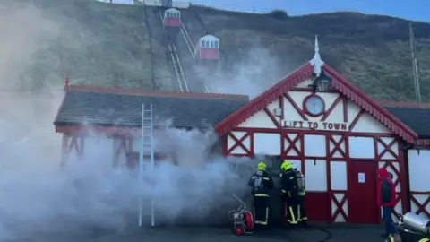 Paul Waugh Saltburn's cliff lift with smoke pouring out of it and fire crews working in front