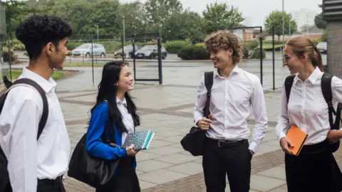 Students wearing school uniform, standing outside their school in Gateshead, North East England at break time. They are standing in a group and bonding with each other.