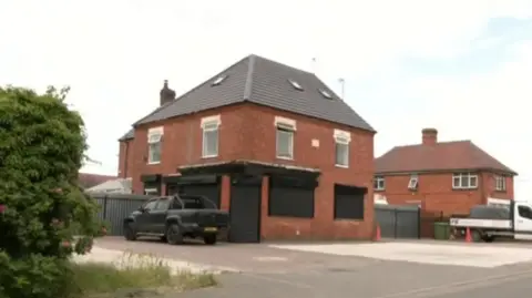 BBC Abattoir site in Arley, Warwickshire. It is a red brick building and the doors and windows have black shutters with a black car parked outside.
