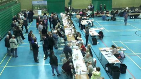 A sports hall filled with people at tables tables counting ballot papers. 