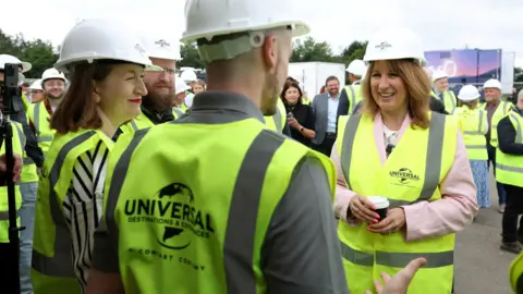 PA Media Rachel Reeves dressed in high-vis with a white Universal hard hat, speaking to others dressed in the same clothes in an outdoor space.
