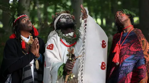 Getty Images A man in white robes with two women beside him, wearing colourful costumes