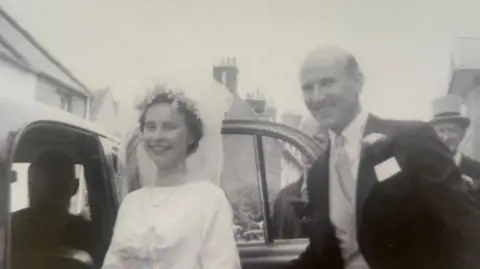 Family handout A vintage black and white image of a bride and groom. The bride weas a white dress and a veil, while the groom is in a black suit and waistcoat. They are getting into a car.