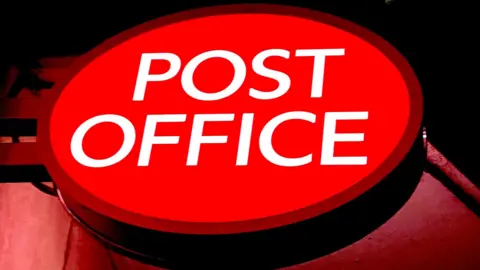 An illuminated red, oval shaped sign with the words "Post Office" in white capital letters.