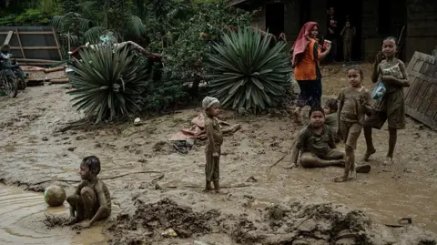 AFP via Getty Images Children play in a muddy puddle in Aceh Tamiang