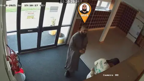 PA Media A CCTV image of Bashir, who has a bald head and beard, stood inside a mosque. 
