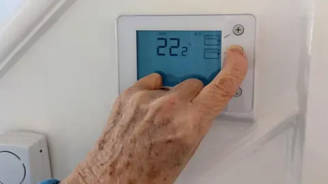 Older person's hand adjusting a thermostat on the wall.