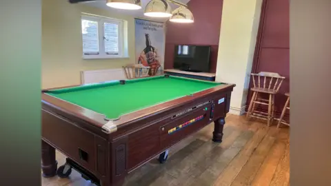 Owen Sennitt/BBC A pool table inside a pub room with gold belled lights above and a TV in the background