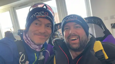 Alastair Crawford Two men smile at the camera wearing winter clothings.