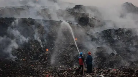 Getty Images Two people spray water onto large smouldering hillsides