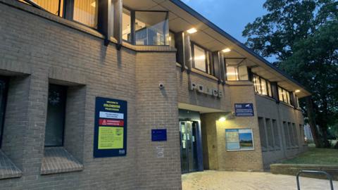 The front of Colchester police station, pictured at dusk with lights on in the offices 