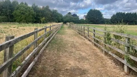 Part of a public right of way in the village of Preston in East Riding of Yorkshire called Nuns Walk. This historic route has been used for years by walkers away from the main roads. It's a long grassy route in between fields and this part of the route has a fence either side of the footpath. 