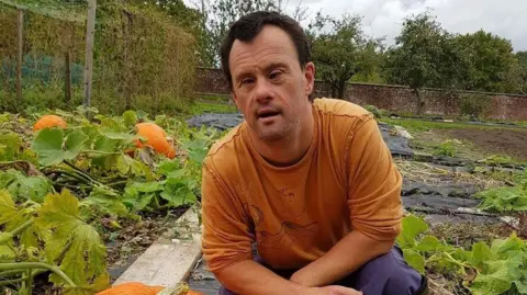 Minstead Trust A man wearing an orange top, kneeling in a pumpkin patch on an allotment