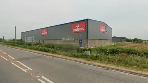 A large rectangular Howdens store in Highbridge. The exterior is grey with the Howdens logo in white on red background