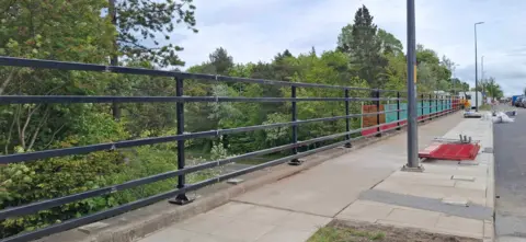 Middlesbrough Council A pavement on a bridge stretching over a dual carriageway is in the centre of the image with black railings to one side 