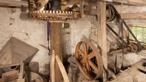 Historic England The interior of a traditional mill, likely the machinery room of an old watermill.