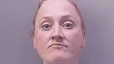 A police mugshot of a woman with scraped-back hair