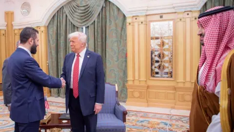 Reuters Syrian interim President Ahmed al-Sharaa (L) shakes hands with US President Donald Trump (C) as Saudi Crown Prince Mohammed bin Salman (R) looks on, in Riyadh, Saudi Arabia (14 May 2025)