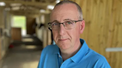 Parent, Asa Neininger, wearing a light blue polo shirt, dark rimmed glasses and short grey hair