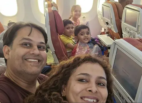 Supplied A middle-aged man sits next to his wife, who has long brown hair in one row of a plane. Across the aisle from the couple are their three children, two young boys and one young girl. They're all smiling.