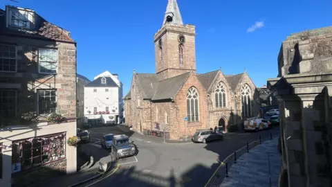 BBC Town church with blue skies in the background. Cars parked on a road. 
