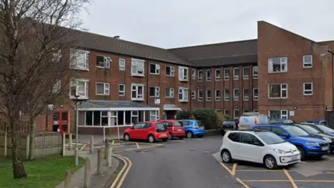 Google Rydal Court in Morecambe, a red brick three storey block of flats with white windows and cars parked outside the front in a car park