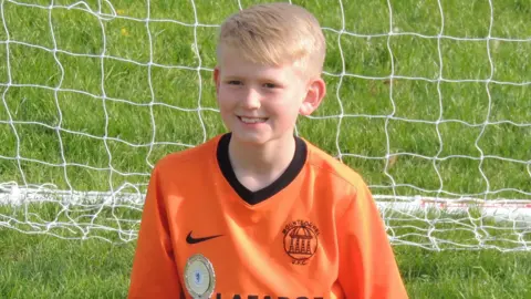 Priestley family Samuel Priestley wearing a orange football shirt in front of a goal