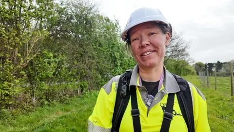 A smiling Steph Barrett giving an interview while out on patrol. She is wearing a helmet and a bright yellow uniform.
