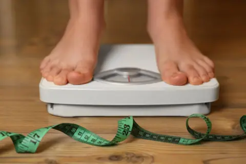 The feet of a child standing on scales with a measuring tape on the floor