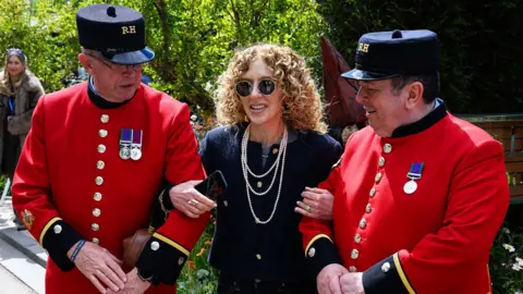 Getty Images British designer Kelly Hoppen poses for photographs with two residents of the Royal Hospital Chelsea on Press Day at the Chelsea Flower Show on May 18, 2026 in London, England.