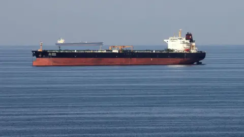 Oil tankers pass through the Strait of Hormuz. Both ships have a red lower section and dark upper section with a white tower. They are heading in opposite directions