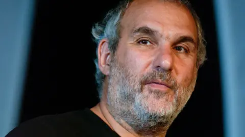 Alan Yentob is seen in a head and shoulders photo against a blue background