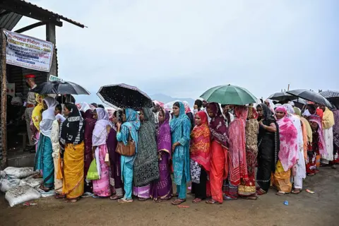 AFP via Getty Images Voters stand in queues to cast their ballots to vote at a polling booth amid rainfall on an island in the middle of the river Brahmaputra during the Assam Legislative Assembly election in the Darrang district on April 9, 2026.