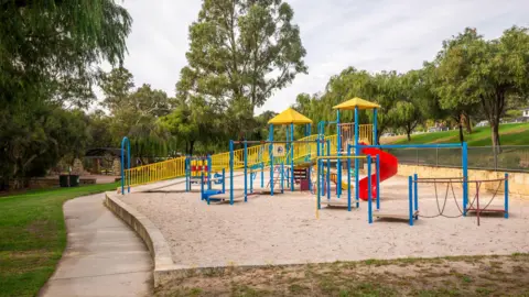 An empty playground surrounded by trees and grass.